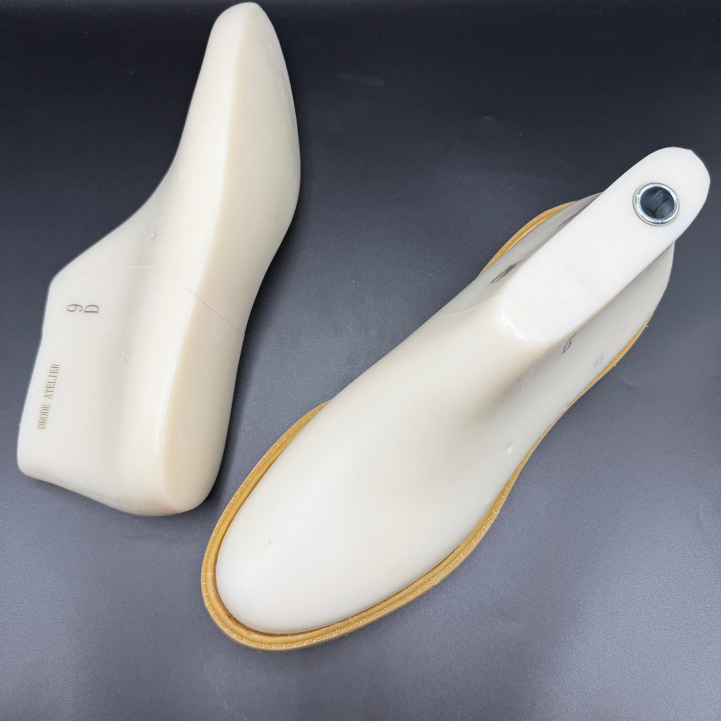 Two white timb boot style shoe lasts on a dark gray background, with one standing upright and the other lying on its side showing a timb boot style sole.