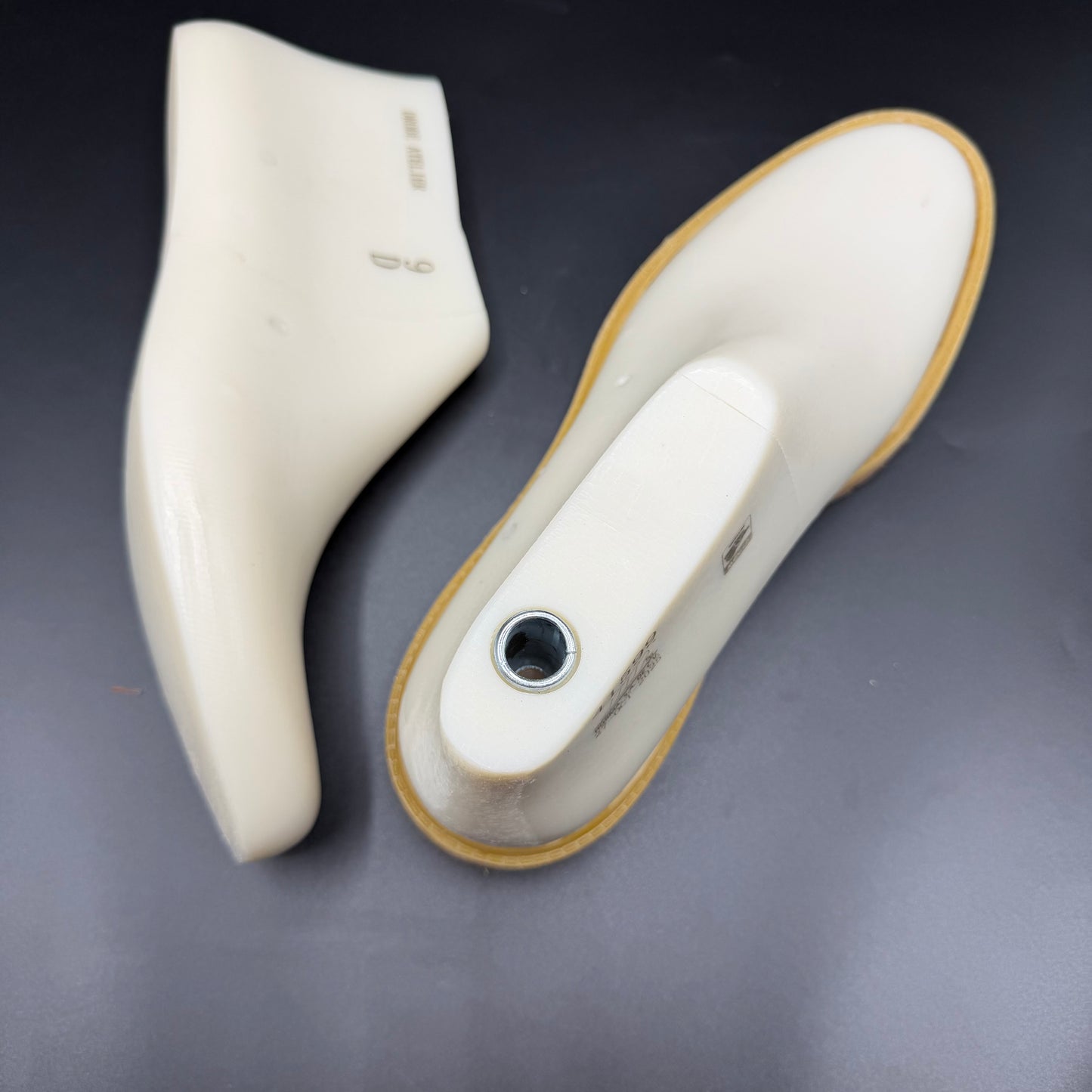 Two white shoe lasts, timb boot style, with a tan rubber sole, displayed on a dark gray background.
